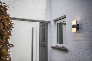 Kinkiet zewnętrzny LED Lutec Cyra 5198102118 IP54 1xLED Aluminium zamontowany na białej ścianie obok drzwi wejściowych.