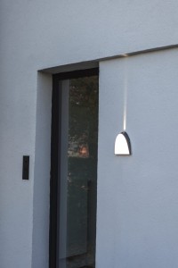 Kinkiet zewnętrzny LED Lutec Apollo 5188801118 zamontowany na ścianie przy drzwiach wejściowych.