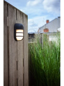 Kinkiet zewnętrzny LED Lutec Bullo 6383001118 zamontowany na drewnianym płocie w ogrodzie.
