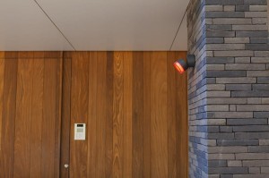 Kinkiet zewnętrzny LED Lutec Dropsi 5010901118 zamontowany na ścianie z szarej cegły.