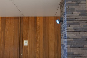 Kinkiet zewnętrzny LED Lutec Dropsi 5010901118 na ceglanej ścianie, włączony.