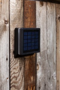 Kinkiet zewnętrzny z czujnikiem Lutec Moze Solar 6943101012 zamontowany na drewnianym płocie.