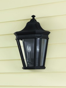 Kinkiet zewnętrzny Elstead Lighting Cotswold Lane FE-COTSLN7-BK IP44 2xE14 Aluminium Czarny na żółtej elewacji.