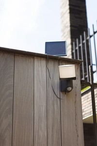 Naświetlacz LED Lutec Sunshine Solar z czujnikiem ruchu zamontowany na drewnianej ścianie.