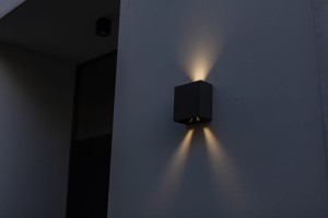 Kinkiet zewnętrzny LED Lutec Gemini 5104003012 IP54 zamontowany na ścianie, emitujący światło.