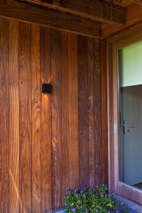 Kinkiet zewnętrzny LED Lutec Gemini 5104003012 czarny IP54 zamontowany na drewnianej ścianie obok drzwi.