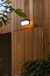Lampa elewacyjna Lutec Fran Solar zamontowana na ścianie drewnianego domu.
