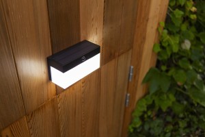 Lampa elewacyjna Lutec Fran Solar z czujnikiem ruchu zamontowana na drewnianej ścianie.