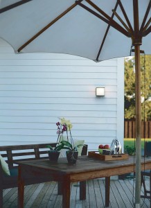 Lampa elewacyjna Elstead Lighting Torsten TORSTEN-SQ IP54 na ścianie białego domu nad tarasem z parasolem.