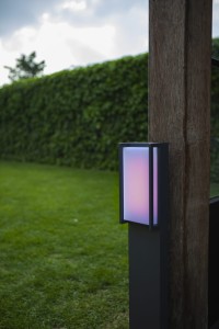 Słupek oświetleniowy Lutec Qubo 7193003118 IP54 1xLED Aluminium Szary zamontowany przy drewnianym palu w ogrodzie.