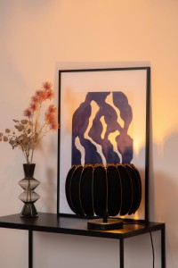Lampa stojąca Spencer. Lucide 1xE27 40W Czarny Filc / Materiał na nowoczesnej komodzie, obok wazonu z kwiatami i abstrakcyjnego obrazu.