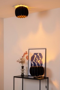 Lampa stojąca Spencer. Lucide 1xE27 40W Czarny Filc / Materiał na konsoli, w tle obraz i wazon z kwiatami.