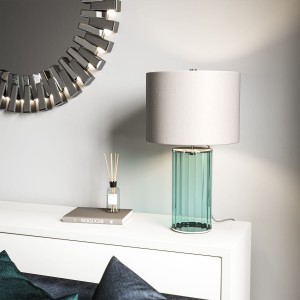 Lampa stołowa Reno Elstead Lighting na białej komodzie obok książki i dyfuzora.