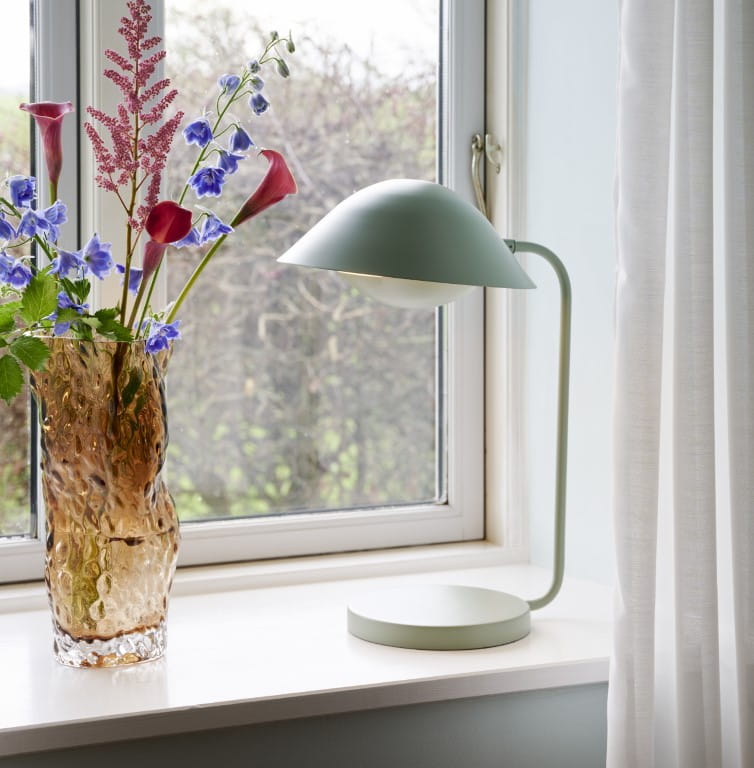 Lampa stołowa FREYA Nordlux 1xE14 40W Metal Zakurzona zieleń na parapecie przy oknie.
