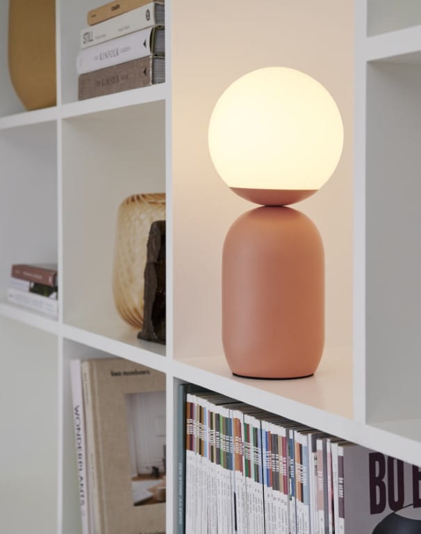 Lampa stołowa NOTTI Nordlux 1xE14 25W Metal Brązowy na półce pełnej książek i dekoracji.